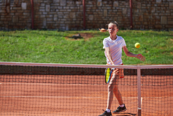 A young girl showing professional tennis skills in a competitive match on a sunny day, surrounded by the modern aesthetics of a tennis court - Foto, afbeelding