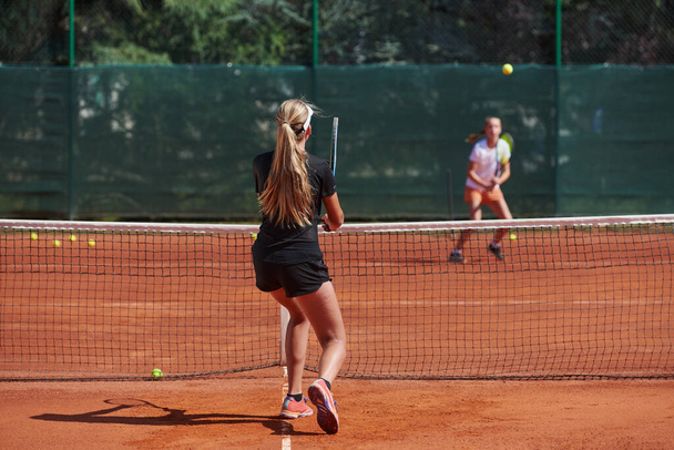 Nuoret tytöt vilkkaassa tennisottelussa aurinkoisena päivänä, osoittaen taitojaan ja innostustaan nykyaikaisella tenniskentällä. - Valokuva, kuva