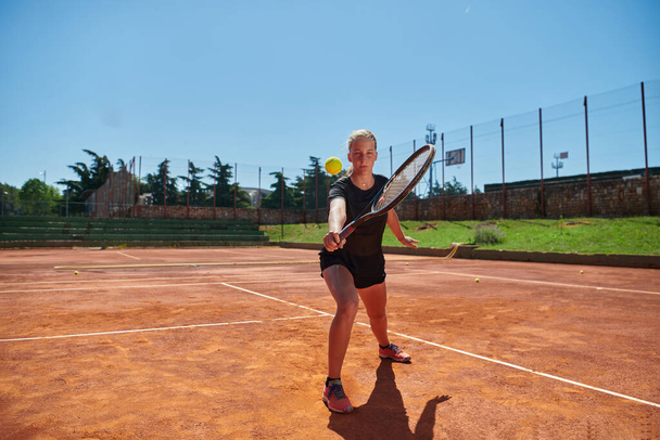 A young girl showing professional tennis skills in a competitive match on a sunny day, surrounded by the modern aesthetics of a tennis court - Foto, afbeelding