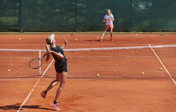 Young girls in a lively tennis match on a sunny day, demonstrating their skills and enthusiasm on a modern tennis court - 写真・画像