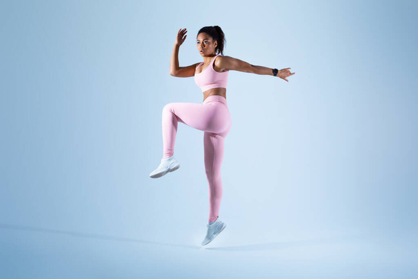 Jeune femme noire dans le jogging et le saut de vêtements de sport en regardant l'espace de copie, le sprint sur fond bleu studio, toute la longueur du corps, bannière, maquette - Photo, image