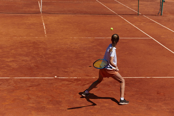 A young girl showing professional tennis skills in a competitive match on a sunny day, surrounded by the modern aesthetics of a tennis court - Foto, Imagem