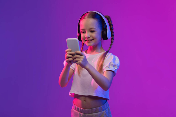 Social Media Influencer. Cute preteen girl recording vlog or live streaming to followers, representing the impact of social media on younger generations, kid using smartphone and wireless headset - Foto, Imagem