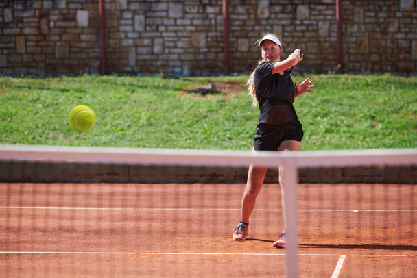 A young girl showing professional tennis skills in a competitive match on a sunny day, surrounded by the modern aesthetics of a tennis court - Foto, Imagen