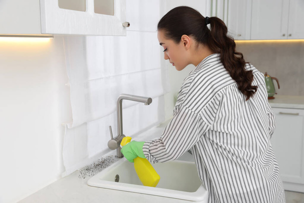 Woman in rubber gloves using mold remover on countertop in kitchen - Fotó, kép