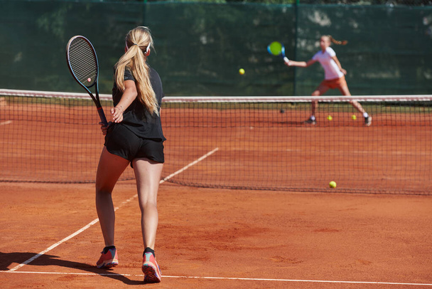 Young girls in a lively tennis match on a sunny day, demonstrating their skills and enthusiasm on a modern tennis court - Valokuva, kuva