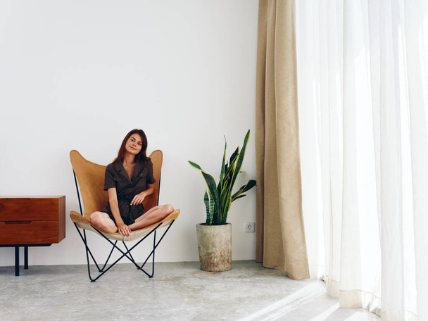 Mujer sentada en un sillón de cuero cerca de la ventana sonriente, moderno y elegante estilo de vida escandinavo, espacio para copiar. Foto de alta calidad - Foto, imagen