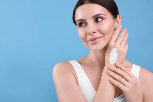 Beautiful woman with smear of body cream on her hand against light blue background, space for text - Foto, Bild