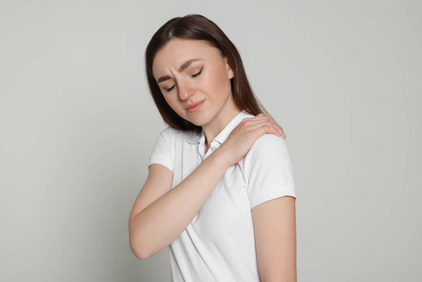 Young woman suffering from pain in her shoulder on light grey background. Arthritis symptoms - Valokuva, kuva