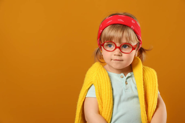Cute little girl in glasses on orange background. Space for text - Foto, imagen