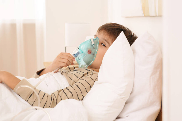 Boy using nebulizer for inhalation on bed at home - Foto, afbeelding