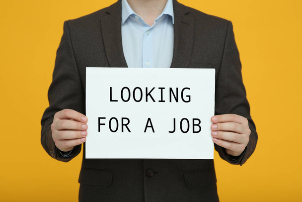 Hombre desempleado sosteniendo letrero con frase Buscando un trabajo sobre fondo naranja, primer plano - Foto, imagen