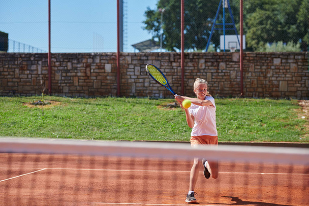 A young girl showing professional tennis skills in a competitive match on a sunny day, surrounded by the modern aesthetics of a tennis court - Foto, Bild