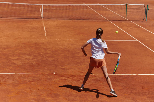 A young girl showing professional tennis skills in a competitive match on a sunny day, surrounded by the modern aesthetics of a tennis court - Valokuva, kuva