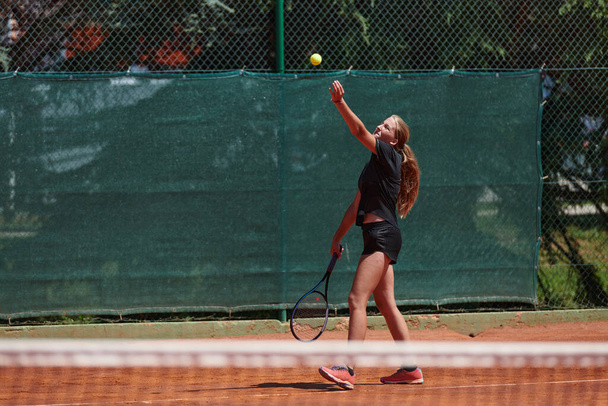 A young girl showing professional tennis skills in a competitive match on a sunny day, surrounded by the modern aesthetics of a tennis court - 写真・画像
