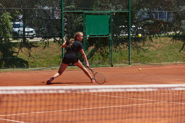 A young girl showing professional tennis skills in a competitive match on a sunny day, surrounded by the modern aesthetics of a tennis court - Photo, Image