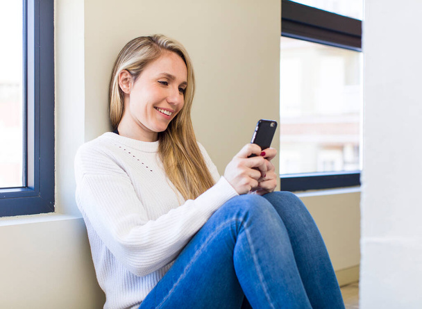 young adult pretty blonde woman using her smartphone at home - Photo, image