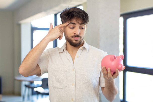 young handsome man looking surprised, realizing a new thought, idea or concept. piggy bank concept - Photo, Image