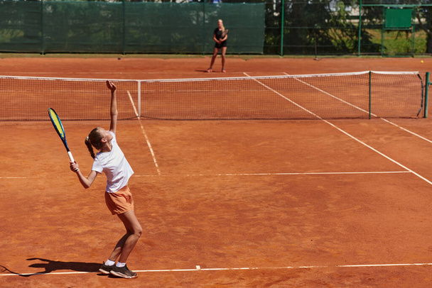 Young girls in a lively tennis match on a sunny day, demonstrating their skills and enthusiasm on a modern tennis court - Фото, изображение