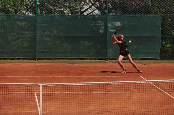 A young girl showing professional tennis skills in a competitive match on a sunny day, surrounded by the modern aesthetics of a tennis court - Фото, изображение