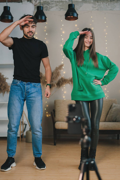 Happy adult man and woman dancing at camera filming video using smartphone on tripod at home. Concept of young blogger. Modern style. - Foto, Imagem