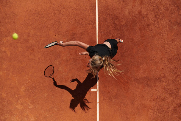 Top view of a professional female tennis player serves the tennis ball on the court with precision and power.  - Фото, изображение