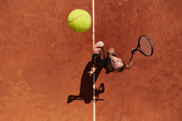 Top view of a professional female tennis player serves the tennis ball on the court with precision and power.  - Φωτογραφία, εικόνα