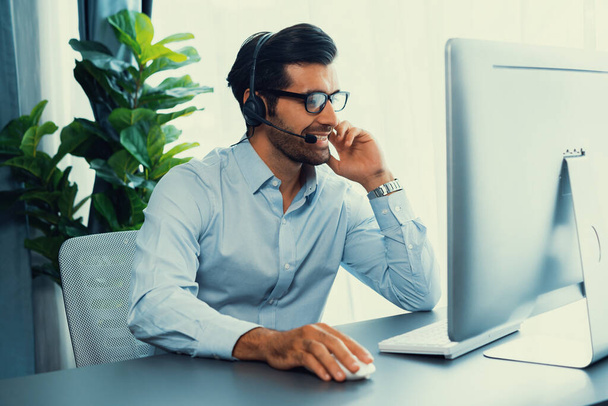 Mies Call Center operaattori tai telesales edustaja istuu hänen toimisto työpöytä yllään kuulokkeet ja harjoittaa keskustelua asiakkaan kanssa, joka tarjoaa asiakaspalvelua tukea tai tehdä myyntiä. kiihkeä - Valokuva, kuva