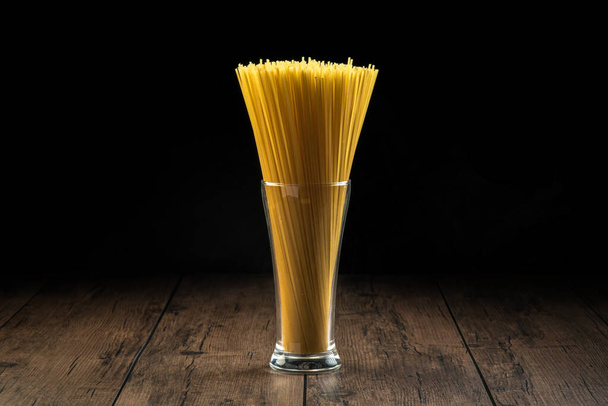 Gli spaghetti vengono messi in un bicchiere che si prepara a cuocere su un tavolo di legno. - Foto, immagini