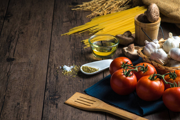 Diverse ingrediënten voor het maken van spaghetti zoals spaghetti, tomaten, champignons, oregano en diverse kruiden geplaatst op een houten tafel, met kopieerruimte. - Foto, afbeelding