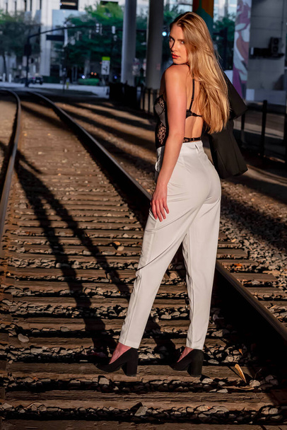 Прекрасная блондинка позирует на железнодорожных путях на закате - Фото, изображение