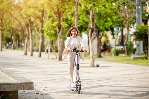 Modieuze dame in pak rijdt elektrische scooter te werken langs kantoorgebouwen. - Foto, afbeelding