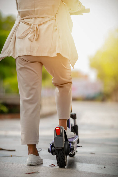 Fashionable lady in suit rides electric scooter to work along office buildings. - 写真・画像