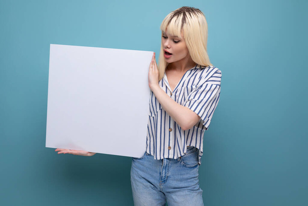 blond young woman in a striped shirt shows a project on a white sheet on a studio background. - Photo, Image