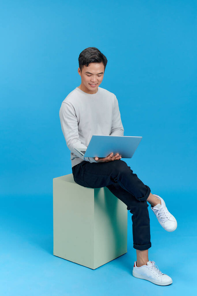 man sitting on a white cube with a laptop computer - Foto, Bild