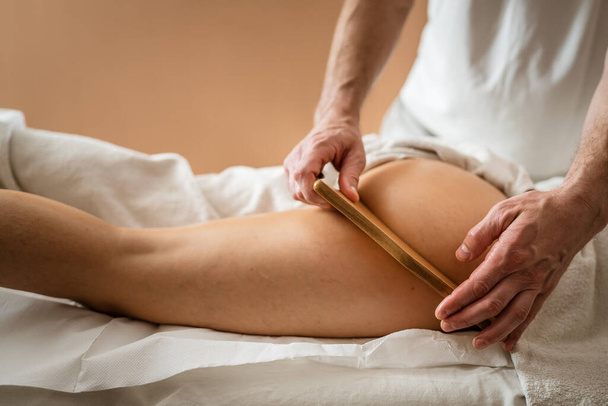 Unknown Caucasian woman having madero therapy massage anti-cellulite treatment by professional therapist holding wooden tools in hands in studio or salon with copy space - Photo, Image