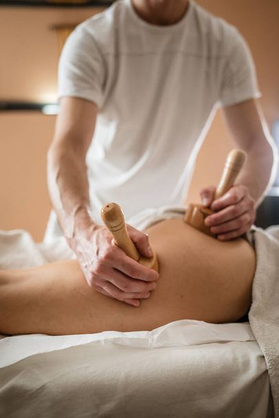 Unbekannte kaukasische Frau bei Maderotherapie-Massage Anti-Cellulite-Behandlung durch einen professionellen Therapeuten mit Holzwerkzeugen in der Hand im Studio oder Salon mit Kopierraum - Foto, Bild
