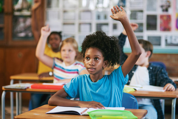 Ενθάρρυνση της δέσμευσης. μια ποικιλόμορφη ομάδα παιδιών που κάθονται στην τάξη του σχολείου τους και σηκώνουν τα χέρια για να απαντήσουν σε μια ερώτηση - Φωτογραφία, εικόνα