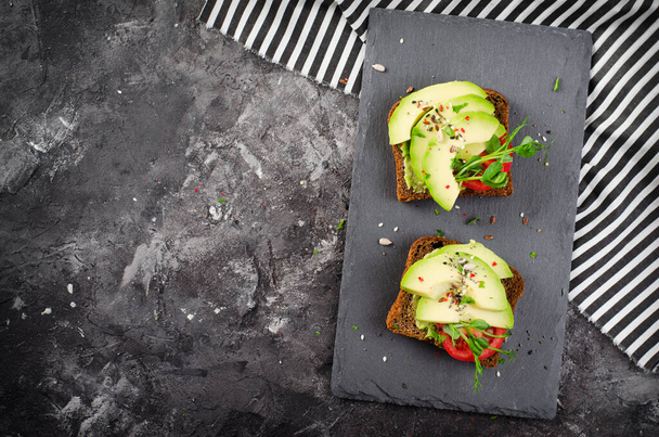 Тосты из авокадо с помидорами, здоровые закуски или завтрак на темно-черном фоне - Фото, изображение