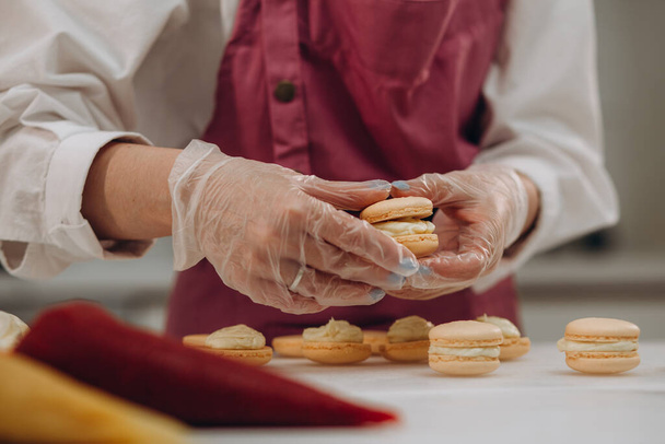 főzés, sütés, és az emberek koncepció - szakács, cukrász táska szorította macaron tészták és a habcsók tejszín tészta shop konyha pergamen papír. - Fotó, kép