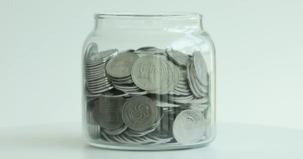 Jarra de vidrio alcancía con monedas girando sobre fondo blanco primer plano película 4k. Concepto de ahorro de jubilación - Imágenes, Vídeo