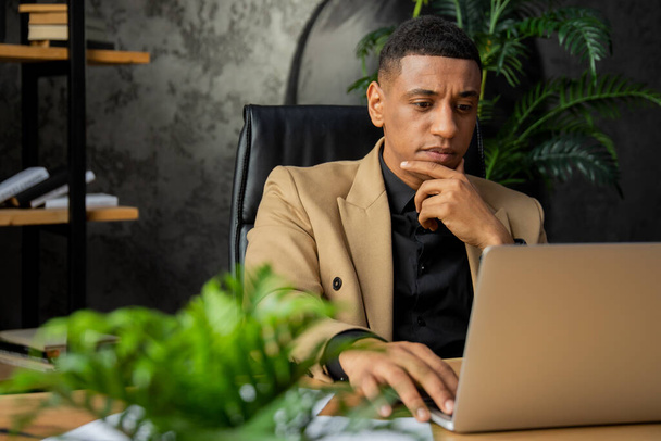 Ein Geschäftsmann mit nachdenklichem Blick sitzt an einem Tisch und blickt auf einen Laptop-Bildschirm. Ein männlicher Geschäftsmann sitzt in seinem Home Office und studiert elektronische Kopien der Jahresabschlüsse seiner Unternehmen auf einem - Foto, Bild