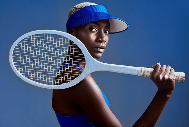 Ze respecteren me als ik het veld oploop. Studio shot van een sportieve jonge vrouw poseren met een tennisracket tegen een blauwe achtergrond - Foto, afbeelding