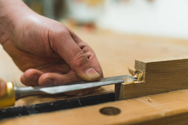 Hands of carpenter carving wood with a chisel to smooth out wooden plank closeup. High quality photo - 写真・画像