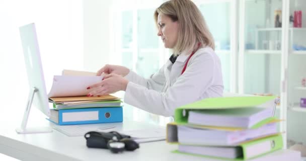 Doctor looking for document among folders and papers at table in clinic 4k movie. Paperwork and bureaucracy in medicine concept - Footage, Video