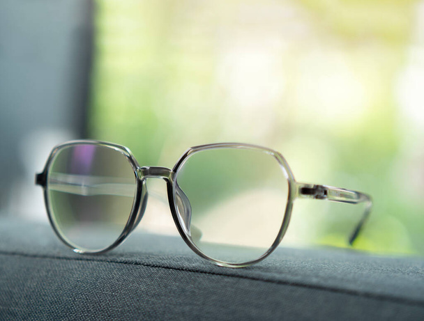 Optische Brillen in einem eleganten grauen Rahmen befinden sich auf einem blauen Stoffkissen in der Nähe eines natürlichen Hintergrundes. Brillengestelle, Gläser, verschiedene Farbkonzepte. - Foto, Bild