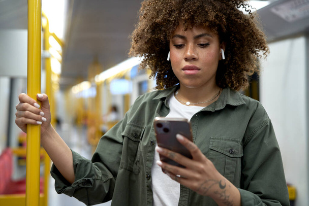 Jeune femme afro debout dans le métro et naviguant sur un téléphone portable - Photo, image