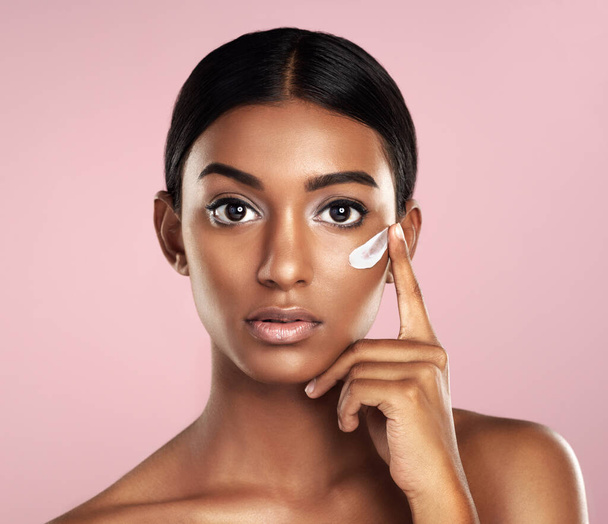 Portrait, skincare and face of woman with cream in studio isolated on pink background. Dermatology, creme cosmetics and serious Indian female model apply moisturizer lotion for skin health or beauty - Φωτογραφία, εικόνα