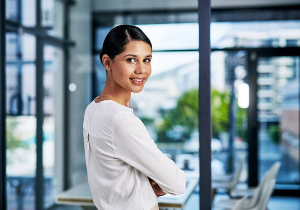 Follow me to my office. Cropped portrait of an attractive young businesswoman smiling while standing with her arms folded in a modern office - Zdjęcie, obraz
