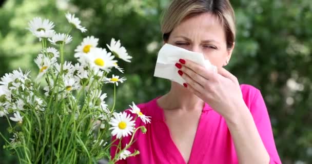 Młoda kobieta z katarem siennym dmuchająca nos w serwetkę w pobliżu filmu o kwiatach rumianku 4k. Koncepcja chorób alergicznych - Materiał filmowy, wideo